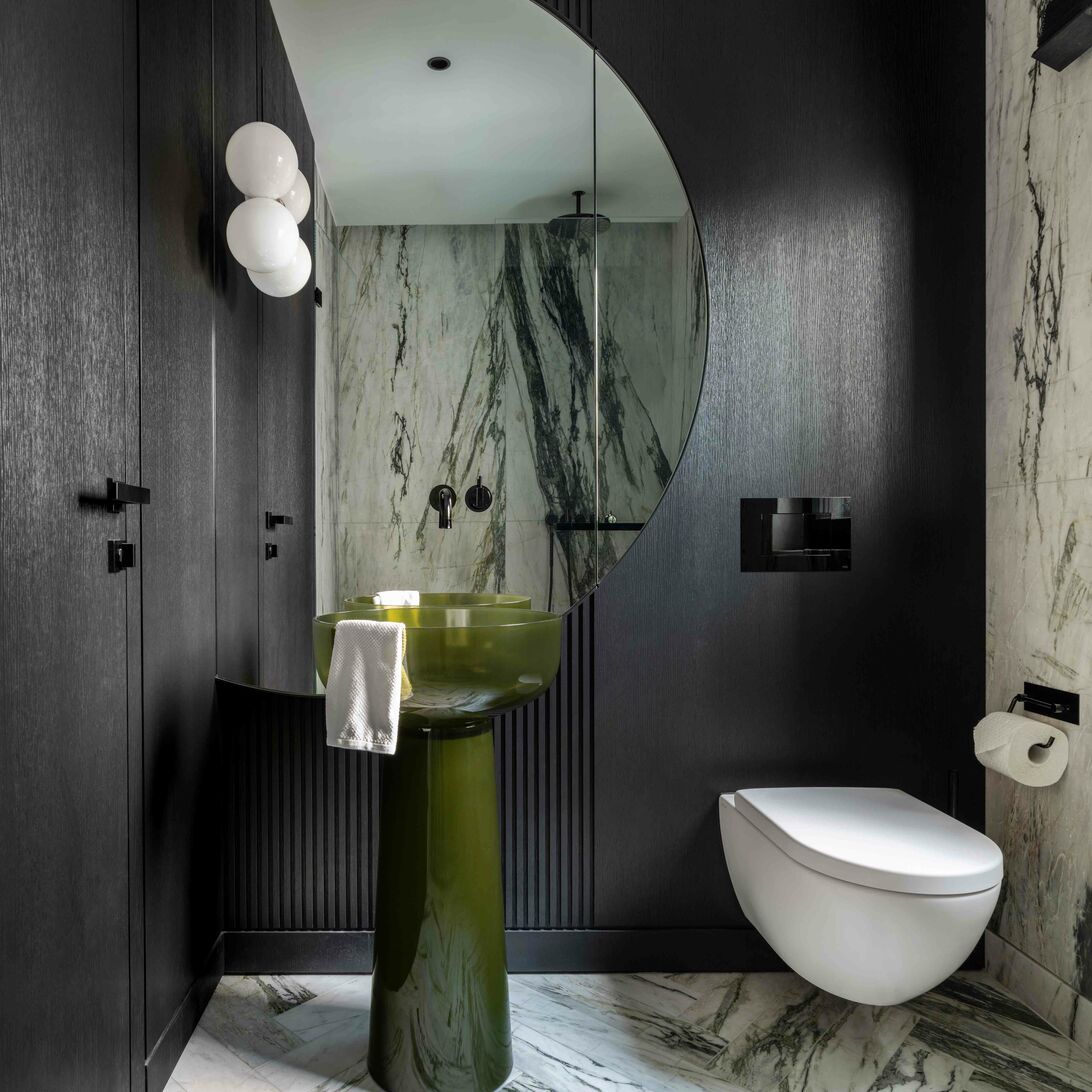 Modernes Bad mit grünem Standwaschbecken, rundem Spiegel, marmorierten Wänden und Boden. Schwarze Akzente und schwebende Toilette vervollständigen das Design. Modernes Bad mit grünem Standwaschbecken, rundem Spiegel, marmorierten Wänden und Boden. Schwarze Akzente und schwebende Toilette vervollständigen das Design.